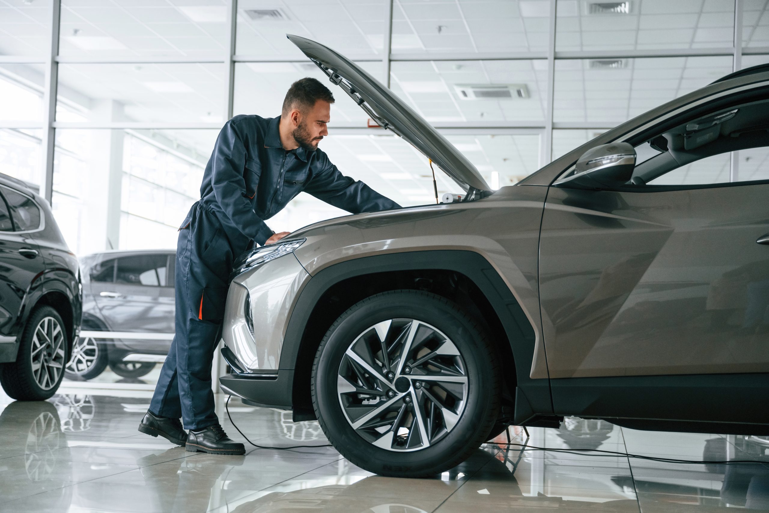 Vehicle technician inspecting SUV under hood indoors